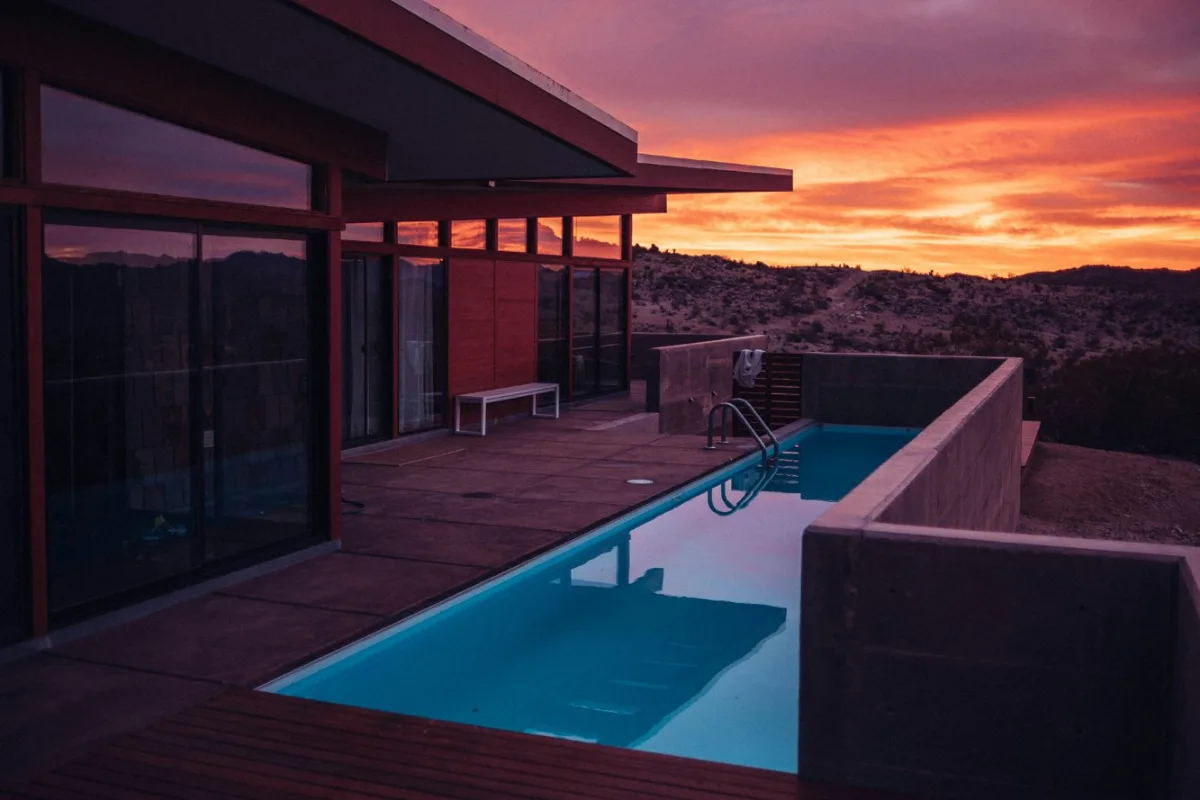 Property exterior converted to a warm dusk scene with a lit pool and sunset sky